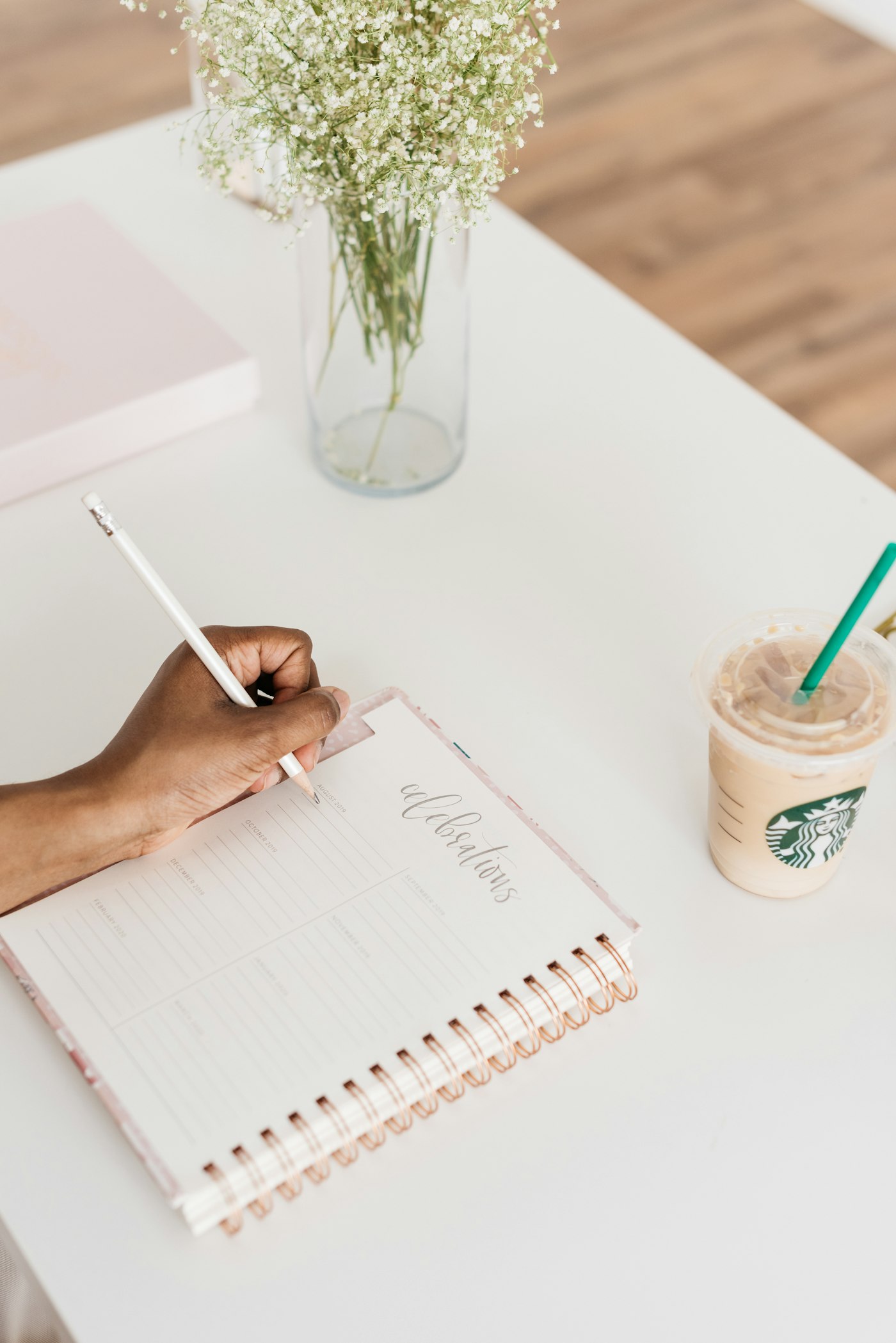 Person writing weekly plans in a notebook beside a cup of coffee on a wooden desk